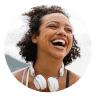 Smiling woman with curly hair and white headphones around her neck, set against a circular coral background. Represents joy, energy, and the supportive Noom community.