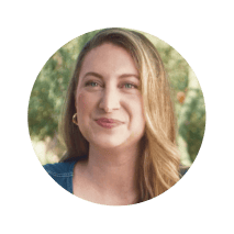 Smiling woman with long blonde hair wearing a denim top, shown in a circular coral frame with a blurred outdoor background. Represents warmth, encouragement, and Noom’s supportive health and wellness community.